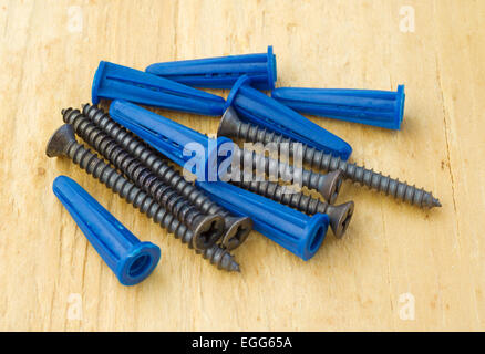 Blue plastic wall anchors with screws on a plywood work bench. Stock Photo