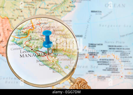 Blue tack on map of Central America with magnifying glass looking in on Managua, Nicaragua Stock Photo