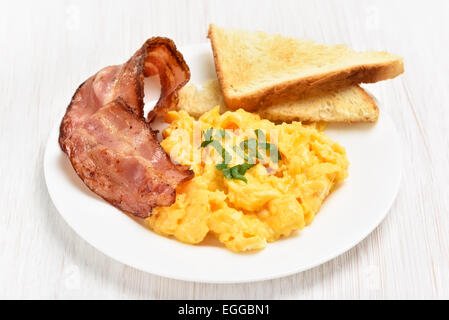 Scrambled eggs with bacon and toasts on white plate, close up view Stock Photo