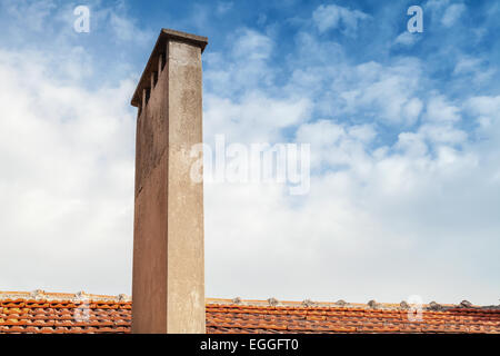 Tall chimney on red tile roof with cloudy sky background Stock Photo