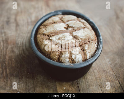 Freshly baked sourdough rye bread in oval bread pan on wooden table Stock Photo