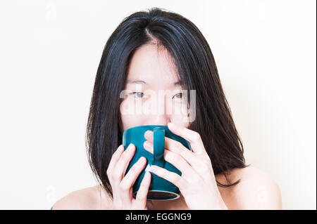 Young asian woman closeup while drinking from blue-green petroleum cup on white background Stock Photo