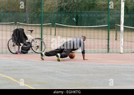 Man doing press-ups with basketball on basketball court in Bedford Park, Bedford, Bedfordshire England Stock Photo