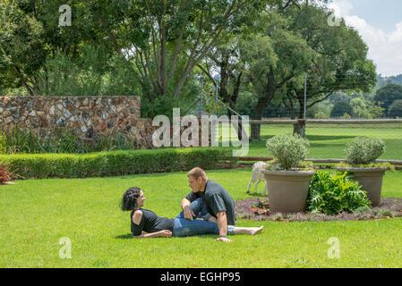 A couple sit on the lawn in their garden enjoying the nice summer weather, while chatting to each other. Stock Photo