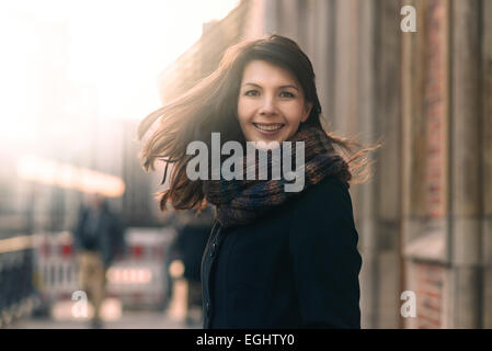 Happy woman with a lovely smile standing in her coat and scarf on an urban street in winter looking at the camera with a joyful Stock Photo