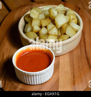 Tapas: Patatas Bravas. Cubes of cooked potato with spicy tomato sauce served in ceramic bowls on a wooden plate Stock Photo