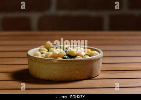 Tapas. Chick pea & spinach cooked in a spicy stock, served in a brown ceramic bowl on a wood tabletop with brick wall background Stock Photo