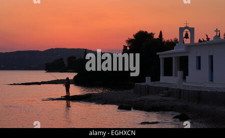 Fisherman at sunset next to Greek church by waterside at Porto Heli, Argolida, Peloponnese, Greece Stock Photo