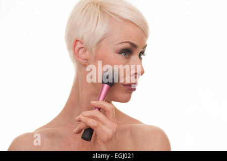 platinum blonde female in her 40s applying make up Stock Photo