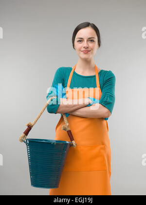 happy confident cleaning lady holding bucket with arms crossed, on grey background Stock Photo