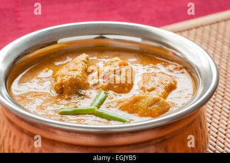 Indian chicken curry served in authentic copper bowl. Green chilli used as garnish. Stock Photo