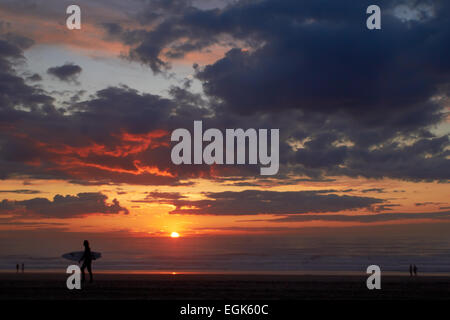 Surfer on the ocean beach at sunset with dark clouds Stock Photo