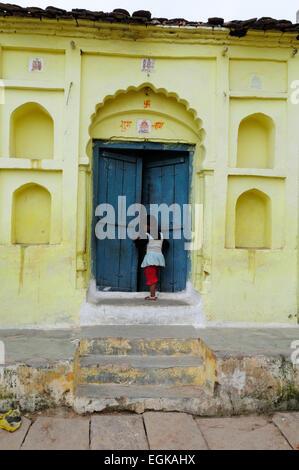 Little Indian girl walking into a yellow and blue painted house Orchha Madhya Pradesh India Stock Photo