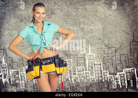 Woman in tool belt standing akimbo against stone wall with sketch of city on it Stock Photo