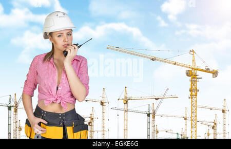 Woman in hard hat and tool belt talking on walkie talkie Stock Photo