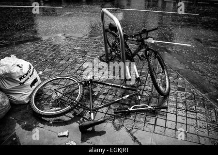 Black and white image of Two bikes secured to a bike stand, one vandalised lying in Manchester street 2015 Stock Photo