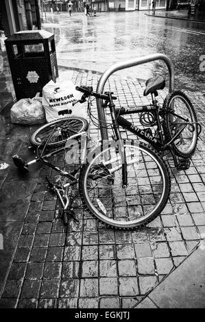 Black and white image of Two bikes secured to a bike stand, one vandalised lying in Manchester street 2015 Stock Photo
