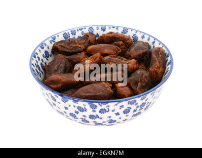Whole dates in a blue and white porcelain bowl with a floral design, isolated on a white background Stock Photo