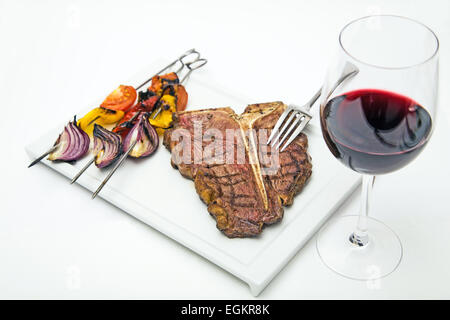 T bone steak on a white plate with grilled vegetable and glass of red wine shot on white Stock Photo