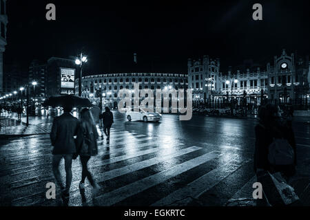 People under umbrellas on a rainy night on the streets of Valencia in Spain on a pedestrian crossing Stock Photo