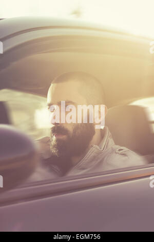 Young handsome man driving his car on a beautiful sunny day. Retro tones. Motion blur Stock Photo