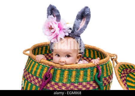 beautiful baby girl sitting in a large basket wearing bunny ears. Stock Photo