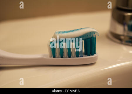 A toothbrush resting on a sink with a swirl of toothpaste of top of the bristles Stock Photo