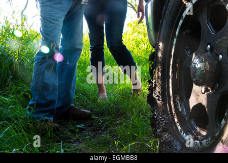 A man and woman standing by a truck tire, covered in mud. Stock Photo