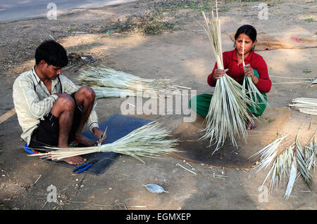 Indian man and woman sitting on the floor making  traditional grass reed brushes Rajasthan India Stock Photo