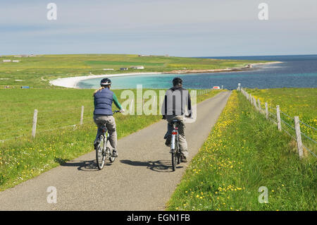 Young man and woman cycling along a quiet road in Deerness, Orkney Islands, Scotland. Stock Photo
