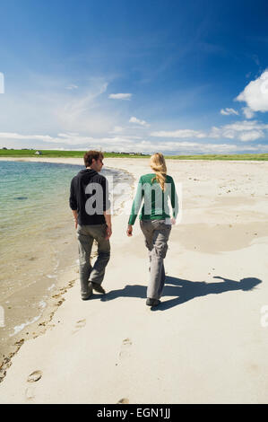 Young woman and man walking along a beautiful sandy beach in summer sunshine, Burray, Orkney Islands, Scotland. Stock Photo
