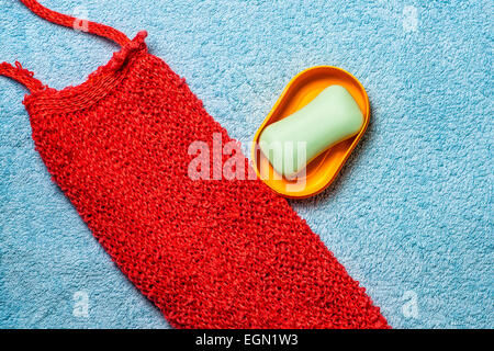Red back scrub, yellow soapbox, green soap on a light blue Turkish towel. The allegory of hygiene. Stock Photo