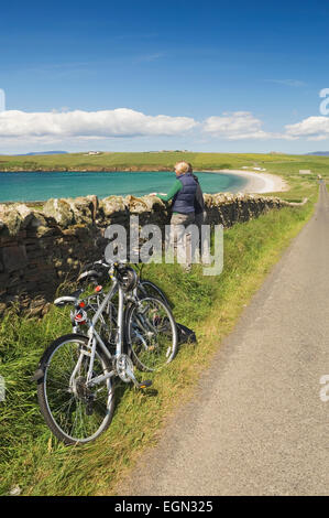 Young man & woman resting beside their bicycles and enjoying the view while cycling on South Ronaldsay, Orkney Islands, Scotland Stock Photo