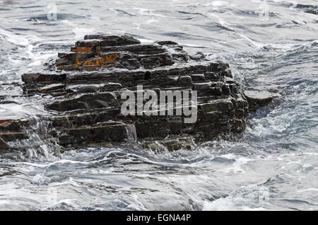 Small waves pour over a layered rock outcrop on the coast of Maine. Stock Photo