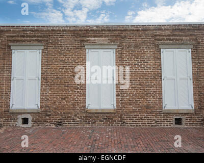 Three white shutters on a red brick building under a blue sky Stock Photo
