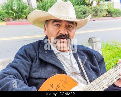 Mexican male guitar player in white cowboy hat playing on a bench on State Street in Santa Barbara, California. Stock Photo