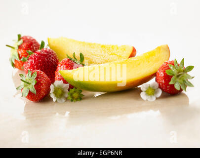 Mango, Mangifera indica. Two slices arranged with strawberries, Fragaria cultivar and flowers, on white marble. Selective focus. Stock Photo