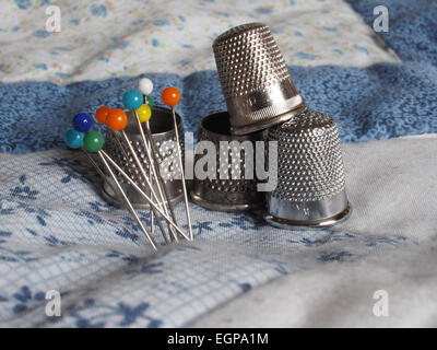 Four different thimbles and a group of coloured pins on some patchwork Stock Photo