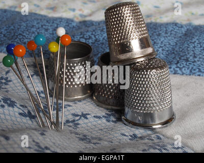 Four different thimbles and a group of coloured pins on some patchwork Stock Photo