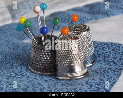 Four different thimbles and a group of coloured pins on some patchwork Stock Photo