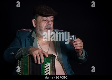 Portrait of an old retired military man who is ready to drink glass of vodka earned while playing accordion Stock Photo