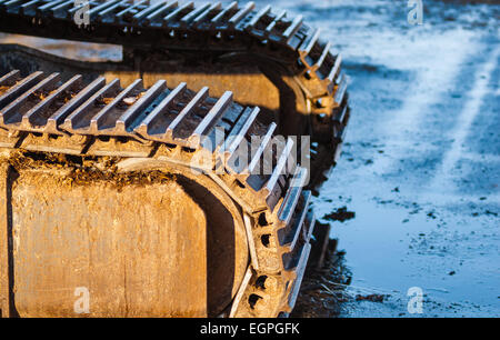 Part of industrial caterpillar tracks in afternoon sun on muddy ground.
