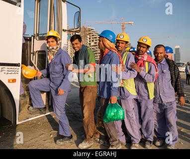 Construction workers queuing to get on bus to living quarters at end of working day in Dubai United Arab Emirates Stock Photo