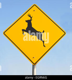 A yellow diamond warning sign with the symbol of a deer in the center against a bright blue sky Stock Photo