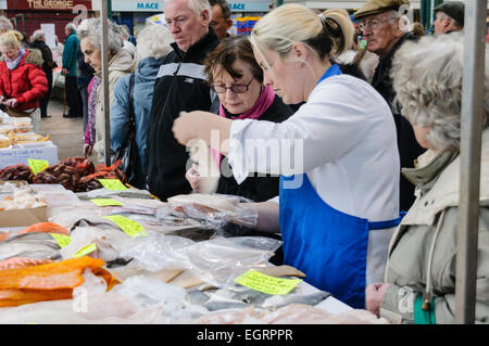 Female fishmonger serves customers at a crowded St. George's Market, Belfast Stock Photo