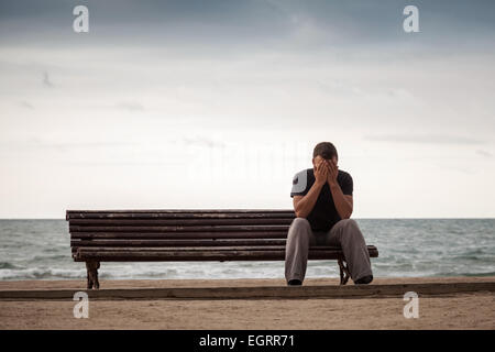 Sad man sits on the old wooden bench on the sea coast. Vintage toned photo with retro toning filter effect Stock Photo
