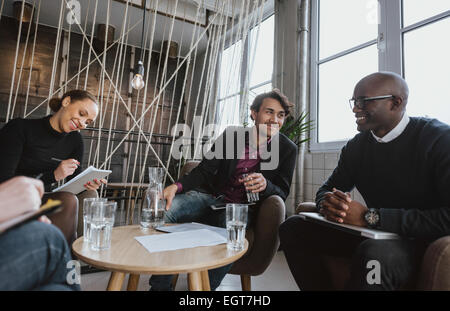 Relaxed young executives having a meeting indoors. Multiracial group of people sitting in office lobby discussing business. Stock Photo