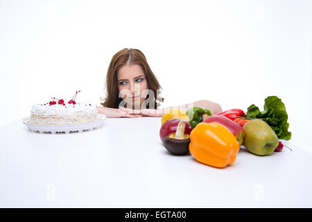 Portrait of a young woman makes a choice between cake and healthy vegetables Stock Photo