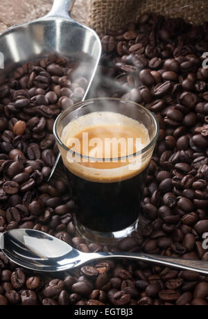 Espresso coffee in glass cup with coffee beans on wooden table. Stock Photo