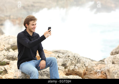 Man using a smart phone in winter on the beach with the ocean in the background Stock Photo